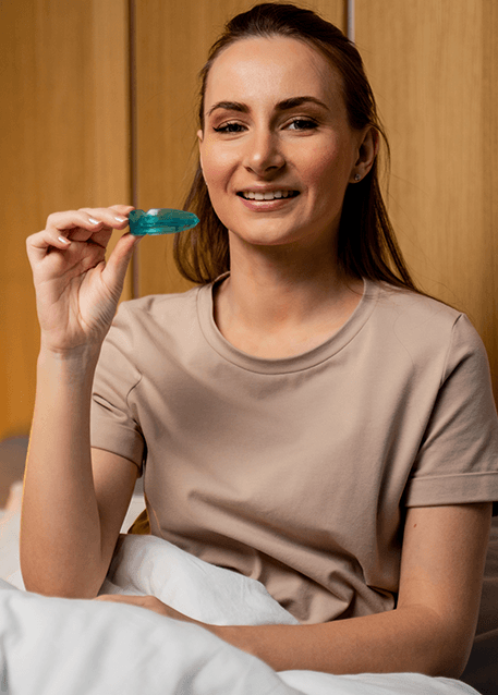 Woman sitting in bed, holding her oral appliance