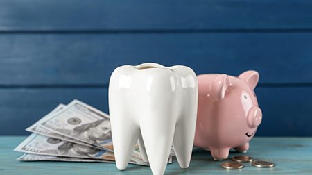 A ceramic tooth, a piggy bank, and money on a light blue wooden table