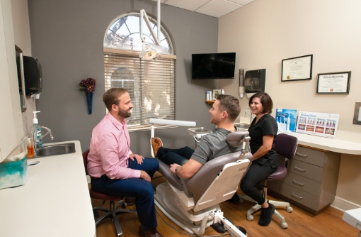 Dentist and team member talking to a man sitting in the dental chair