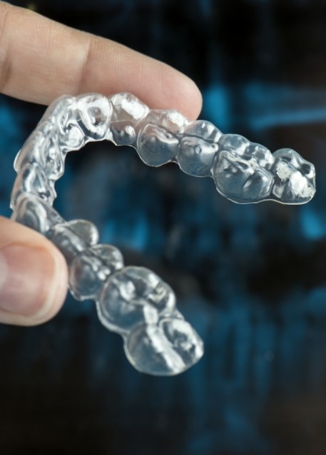 Hand holding an Invisalign aligner with dental x ray in background