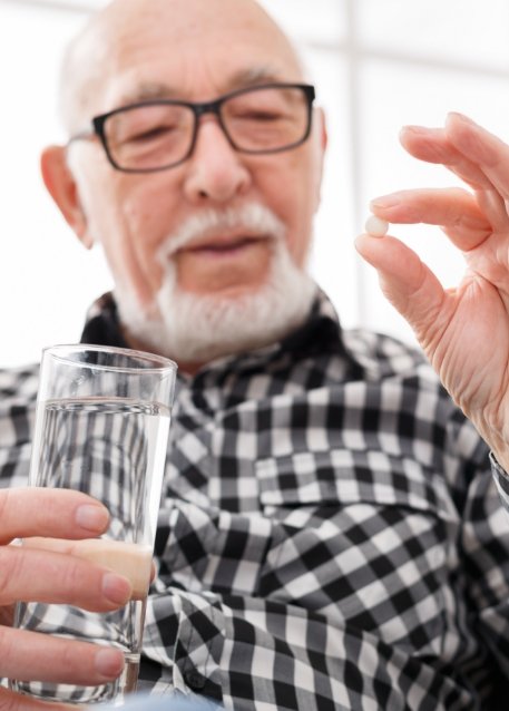 Older man holding a white pill and glass of water