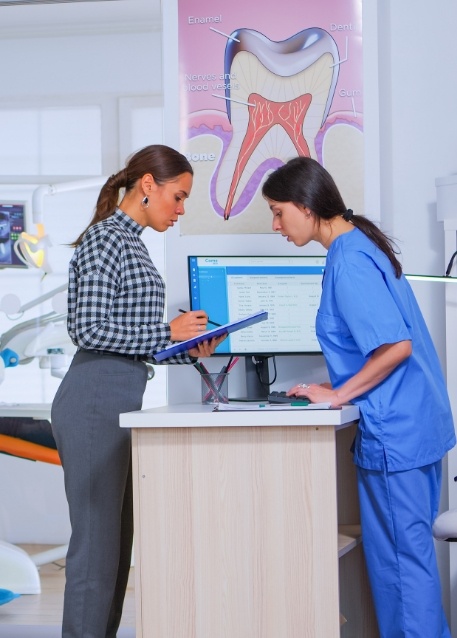 Woman signing a clipboard next to a dental team member