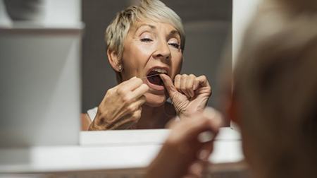 Woman flossing her teeth in mirror