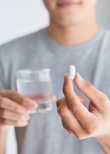 Person holding a white pill and a glass of water