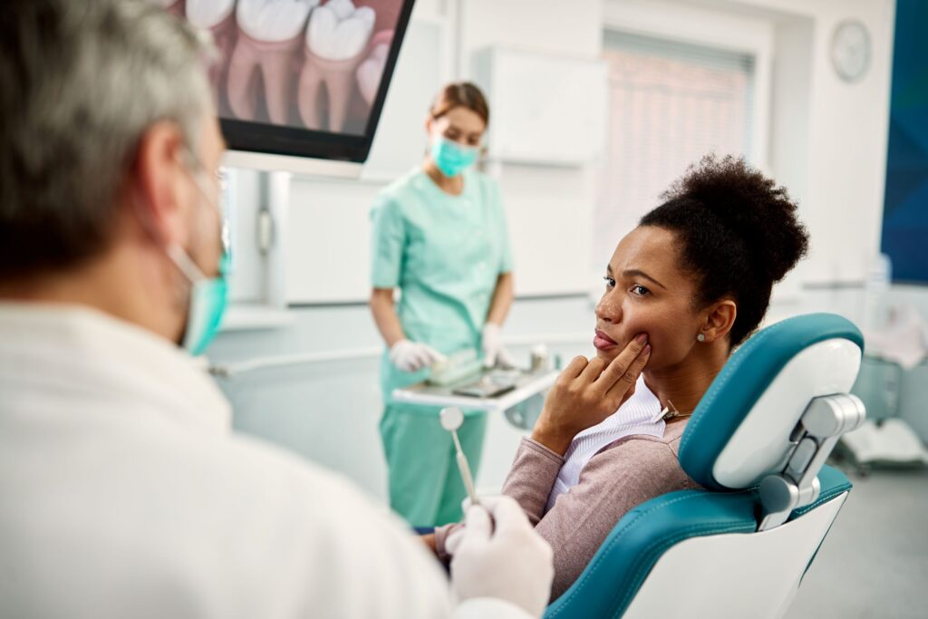 Woman in dental chair listening to dentist holding 2 fingers to sore jaw